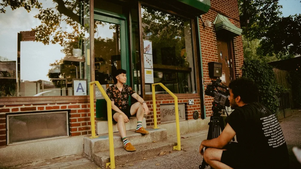 BTS photo of chris filming Larry's owner Tuan on the front step of the business.